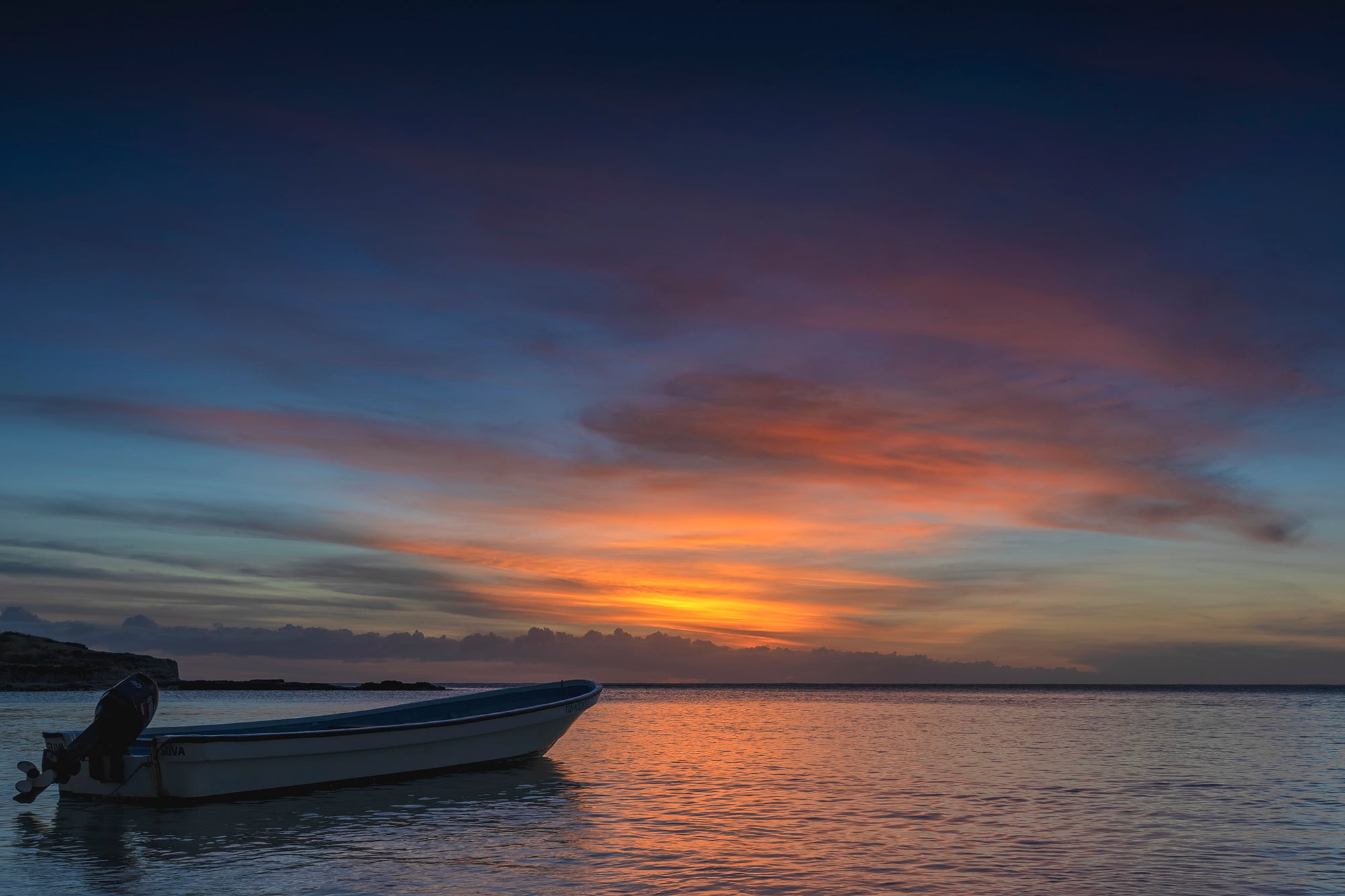 An image of a sunset in Fiji with a local fishing boat sitting alone in the forground.